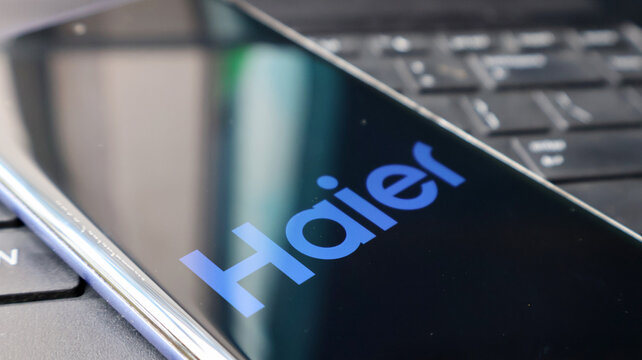 A smartphone with the Haier logo on its screen placed on a laptop keyboard