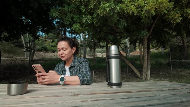 Woman Relaxing Outdoors and Using Smartphone at Picnic Table in Nature
