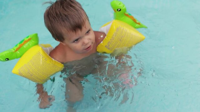 Kid in oversleeves swims in the pool in the yard