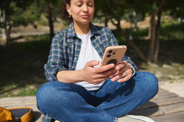 Fototapeta premium Woman sitting cross-legged outdoors using smartphone in sunny park
