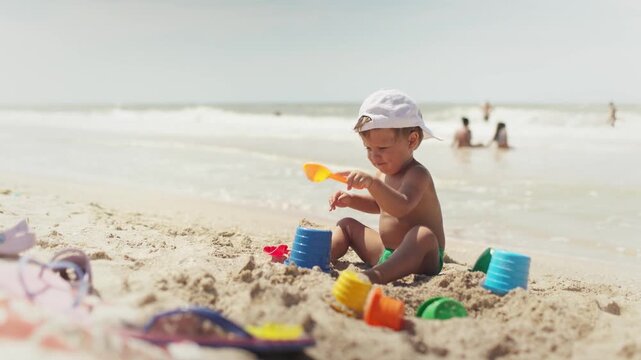 Boy playing with toys on the beach building beads and turrets smiling at someone behind the scenes on summer vacation