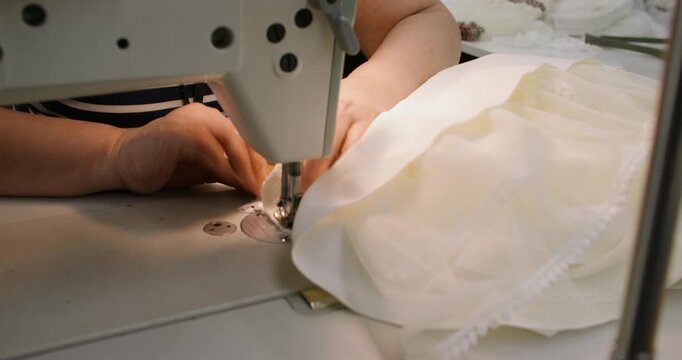 Seamstress work. Custom garment. Woman hand stitching white textile lace clothes on professional electrical manufacturing equipment.
