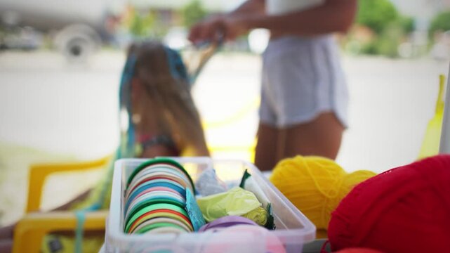 Many threads and ribbons lie on the table against the background of a girl whose African braids are weaving