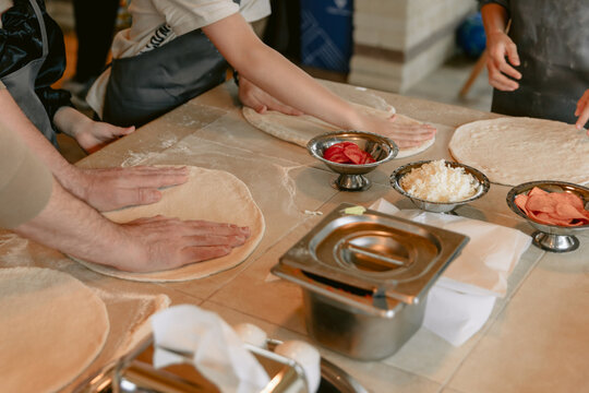 Hands preparing pizza dough with fresh ingredients in kitchen cooking class