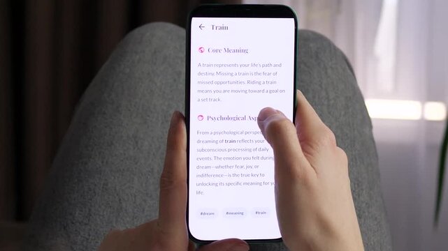 Close-up of a person reading a dream interpretation app on a smartphone. Screen explains the psychological meaning of dreaming about trains. Concept of subconscious analysis, mindfulness, and self