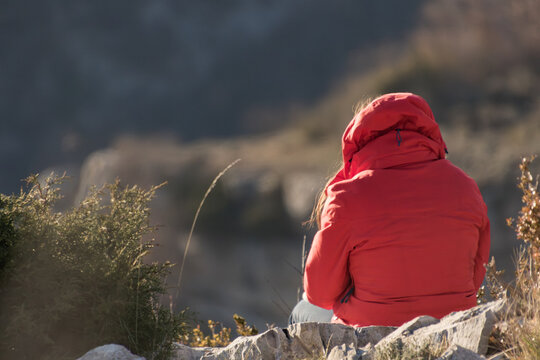 Femme assise de dos au bord d&rsquo;une falaise en doudoune avec capuche rouge
