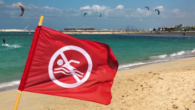 Red flag on Dubai beach warning swimmers with golden sand, turquoise water, and sunny coastal environmen