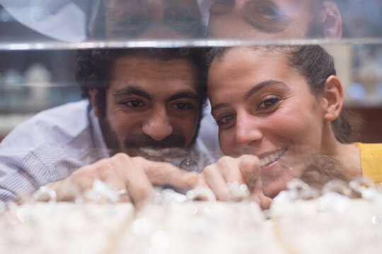 Middle Eastern couple choosing wedding rings together at a jewelry store, smiling and excited with friends