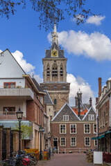 Fototapeta premium Street view in Delft, Netherlands, towards the church. Historic brick architecture and stone paving under cloudy gray sky