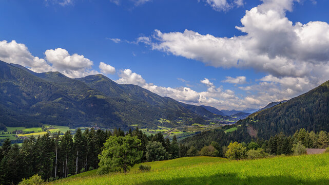 Alps, Styria, Austria, panoramic view of mountain valley. Green hills and forest under partly cloudy sky in central region