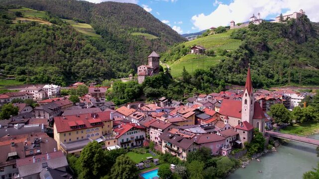 Italy South Tyrol 4k aerial drone pan of Chiusa Klausen with Isarco river and bridge. Scenic cinematic view of historic Branzoll castle Sabiona monastery & vineyards. Iconic Alpine village Hidden gems