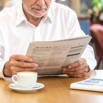 Senior man in a white shirt reading a newspaper over morning coffee in a cafe. This peaceful scene captures the essence of a relaxed retirement and staying informed in the digital age.