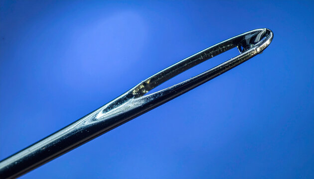 Extreme macro photography captures the intricate detail of a needles eye against a blue background. Representing precision and focus in tailoring, sewing, crafts, and business metaphors.