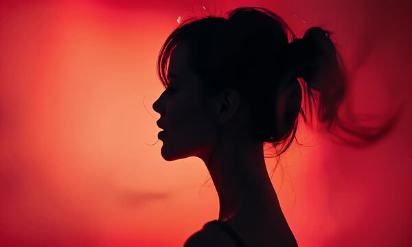 A woman's silhouette faces left against a vibrant red background with her hair in a ponytail.