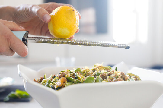 Hand grating fresh lemon zest over vegetable pasta
