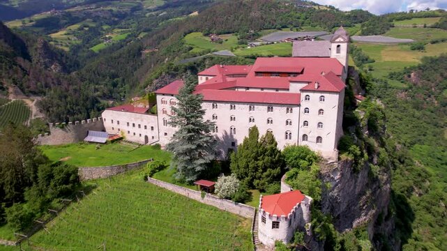 Chiusa Klausen Italy 4k aerial drone pull back video of Sabiona Monastery on cliff rock. Scenic South Tyrol landscape revealing Isarco valley and vineyards. Medieval architecture in Dolomites Alps
