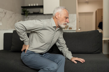 Fototapeta premium Elderly man feeling severe back pain, sitting on a sofa