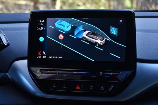 The screen shows a close-up of the digital instrument cluster, which displays active driver assistance systems such as IQ.DRIVE. The image showcases modern automotive technology and safety. 