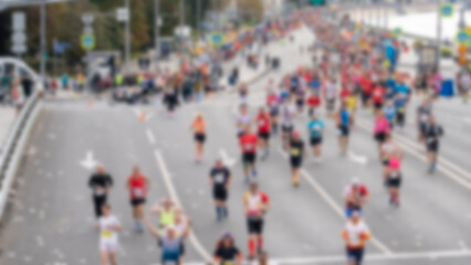 Obraz premium Blurry urban street scene with many runners moving forward. Diverse participants in athletic wear show effort and focus. Spectators line the road, adding community energy