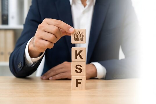Business professional assembling wooden blocks spelling "ksf" with a team icon on top, representing key success factors.