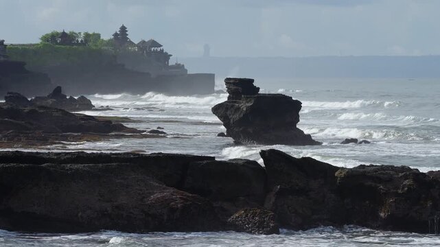 Rocky Shoreline With Distant Tanah Lot Temple, Exposed Rock Pools And Tide Patterns, Greening Clifftop And Geological Outcrops, Contemplative Coastal Scene, Tanah Lot temple, Bali, Indonesia