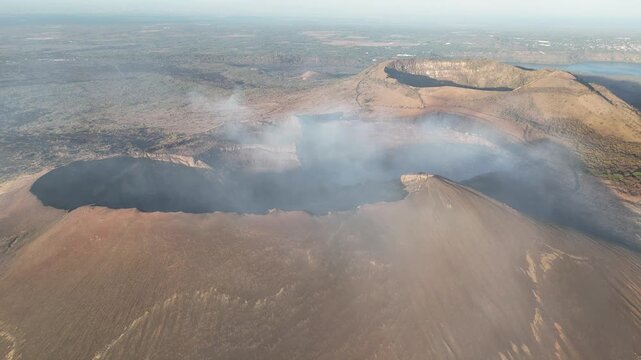 Smoke rises from the crater of an active volcano in Nicaragua. The landscape shows signs of volcanic activity and barren ground around the area.