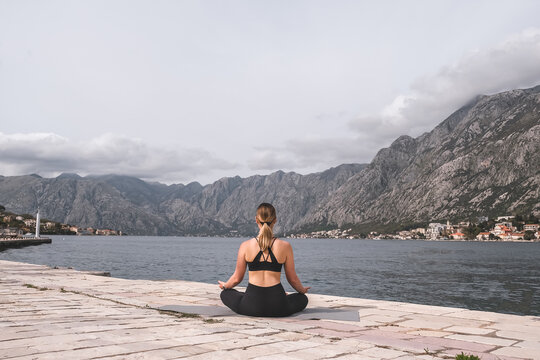 Young woman practicing advanced outdoor yoga pose on mat by the sea with mountain view, wellness and mindfulness concept, balance, flexibility and healthy active lifestyle.