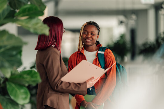 Female professor mentoring young university student in campus hallway, offering educational advice and consultation