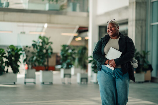 Black businesswoman smiling, carrying laptop in modern office, portraying success and inclusive workplace environment