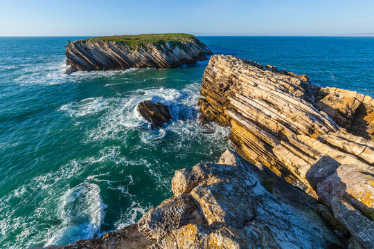 Dramatic tilted rock formations and layered cliffs rise from the blue atlantic  ocean