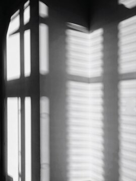 Minimalist rectangular patterns of light and shadow, created by window blinds, fall across a column and smooth architectural wall, offering generous copy space.