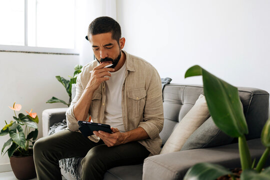 Man sitting on sofa at home using tablet, browsing, reading or communicating in a bright living room environment with natural light.