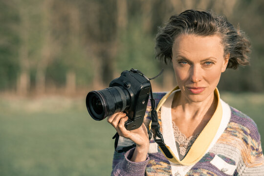 Female photographer holding camera outdoors with confident expression