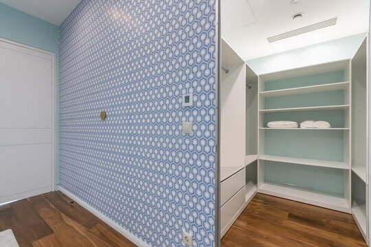 A room features a blue patterned wall with a cozy design. An open closet shows neatly stacked towels and empty shelves, creating a spacious look