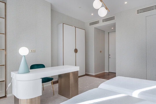 A room shows a simple design with a desk, chair, and wardrobe. The walls have geometric patterns, and the flooring looks clean and bright. This space is likely used for resting or working