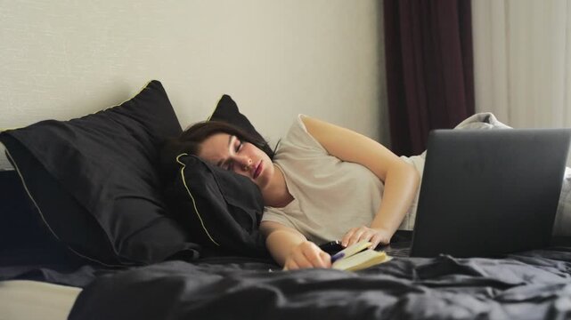 Woman fallen asleep with her computer on the bed, holding mobile phone