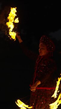 Mesmerizing night fire performance with traditional costume and swirling flames creating dramatic light trails against a dark outdoor background