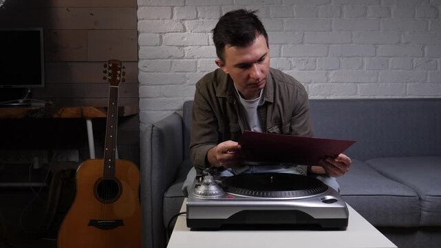 Man sitting on sofa flipping through a vinyl album cover, preparing a vintage turntable session in a cozy living room, enjoying a relaxed weekend hobby at home