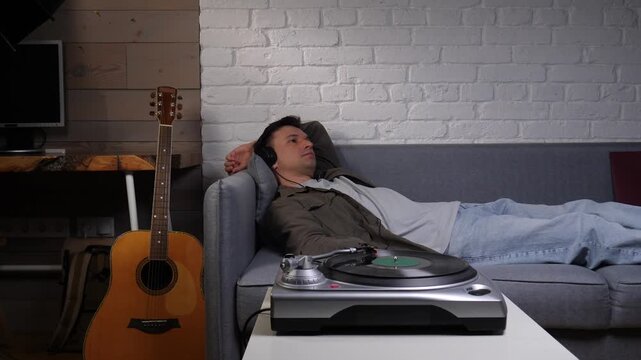 Man relaxing on a cozy sofa wearing headphones, enjoying vinyl from a record player in a peaceful living room, soaking in quiet weekend leisure and vintage hi fi comfort