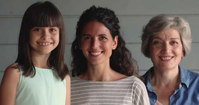 Headshot portrait smiling granddaughter, adult mother and grandmother looking at camera, posing indoors, representing strong multigenerational family relationships, diversity, generational continuity