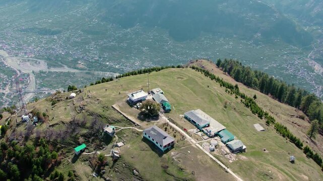 Aerial view of Bijli Mahadev hilltop in Himachal Pradesh with temple complex, telecom tower, and snow mountains, popular travel destination