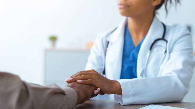 A doctor meets with a patient at a medical office. The doctor has her hand on the patient's hand. They discuss health concerns. The setting is bright and has a neutral design.