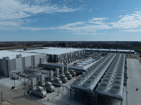 Aerial view of a large AI data center with industrial cooling systems, servers, and infrastructure in a modern high-tech facility under a clear blue sky.