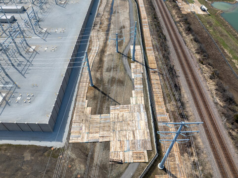 Aerial view of timber construction mats forming temporary access roads for power line installation beside substation, transmission towers, and railway corridor.

