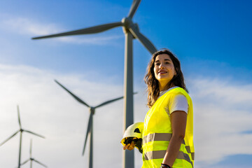Woman engineer holding helmet and smiling, standing in front of wind turbines © Ivi - Powerlightss