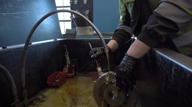 Close-up of cleaning heavy machinery parts with fuel. Mechanic washing industrial gear from oil and grease in a workshop sink. Manual degreasing process for automotive repair.