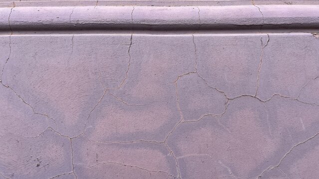 Close‑up of a pale lilac plaster facade with fine cracks and worn paint beneath a simple horizontal molding, showing subtle aging and texture of a historic exterior wall