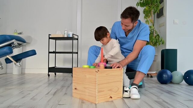 Child with disability performing motor skills exercises with physiotherapist using educational game. Pediatric rehabilitation, coordination development, therapy and healthcare concept. High quality 4k