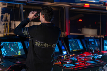 Officer looking through binoculars on ship bridge at night © DMITRII RYBALKA