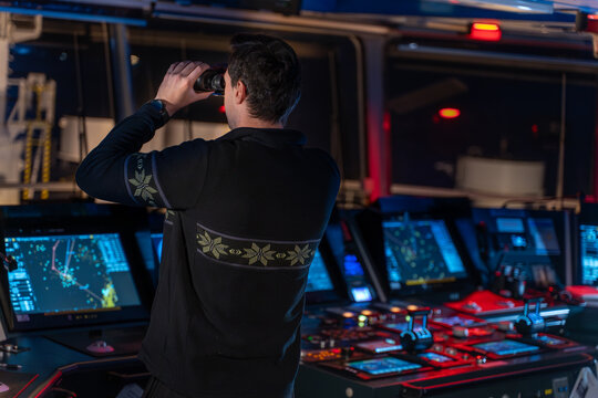 Officer looking through binoculars on ship bridge at night